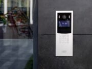Scs-sentinel.com, sécurité connectée et solutions intelligentes pour la maison Entrance doorbell in a multi-apartment building, with a video surveillance camera, on a dark wall